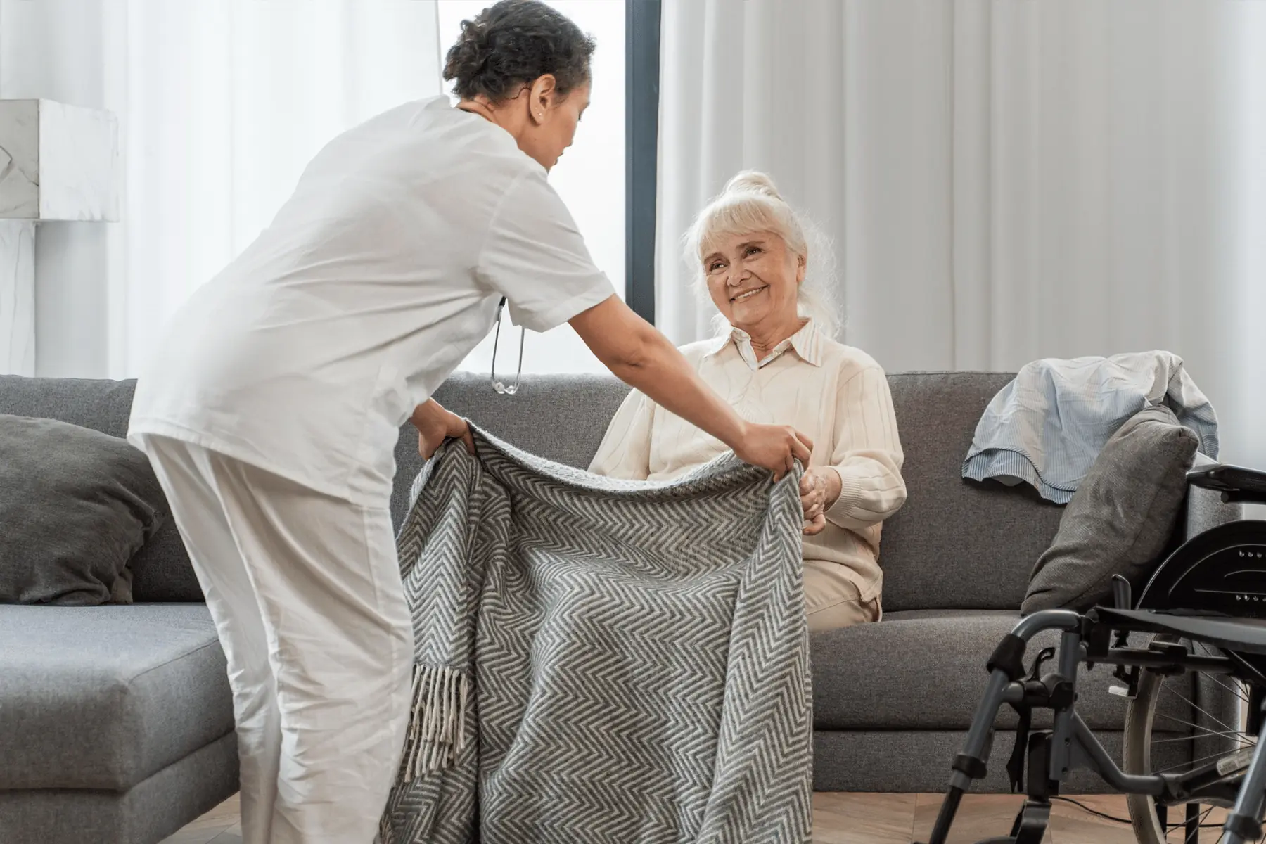 Une préposée dépose une couverture sur les genoux d'une résidente assise dans un fauteuil.