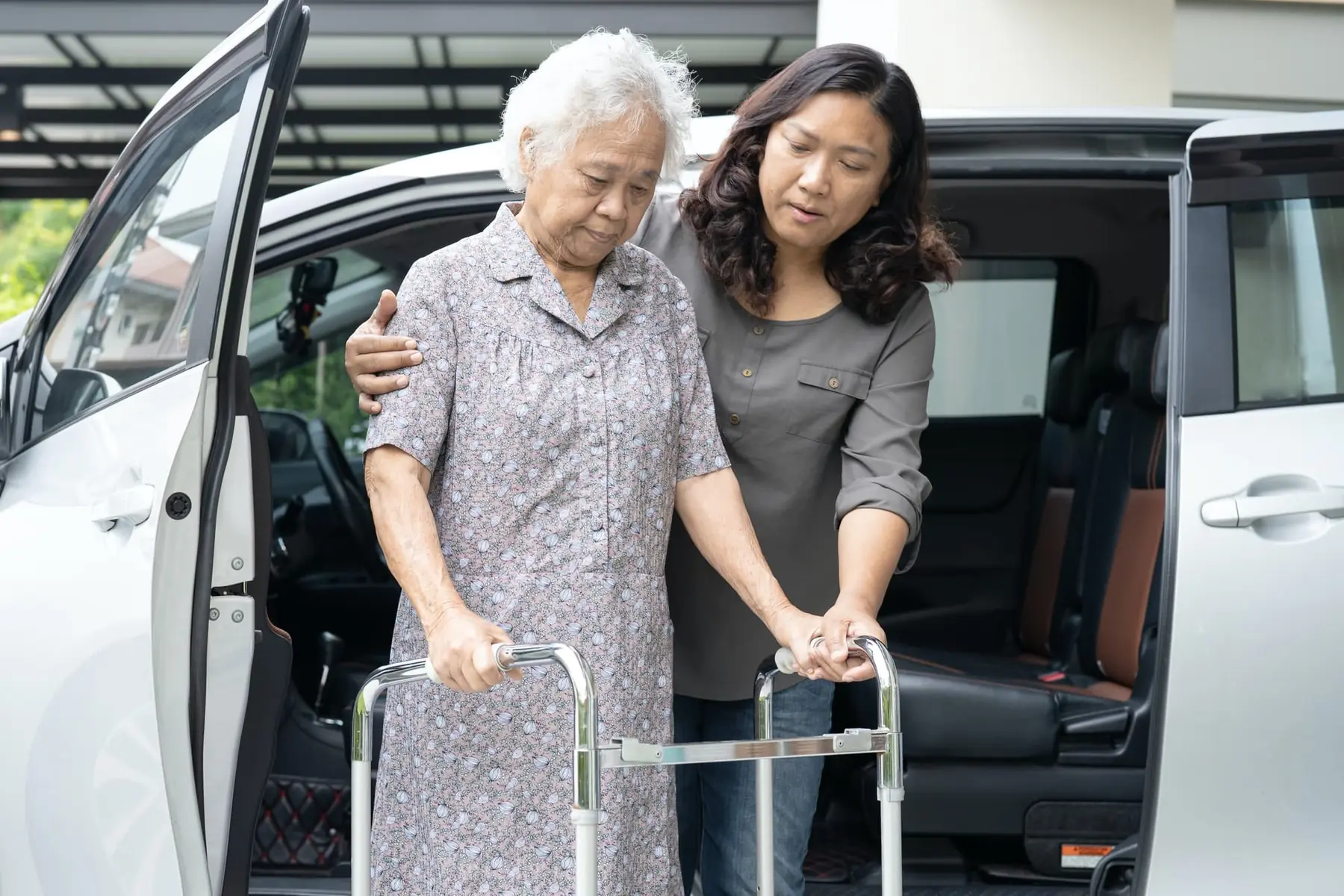 Une résidente descend d'une voiture avec sa marchette, accompagnée par une personne qui la soutient.